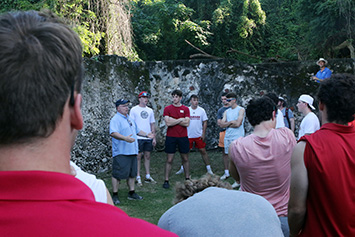 Prof Dan Rogers (left rear) and Jackson Woehr ’26 (rear center in  red shirt) present class information at the sugar mill.