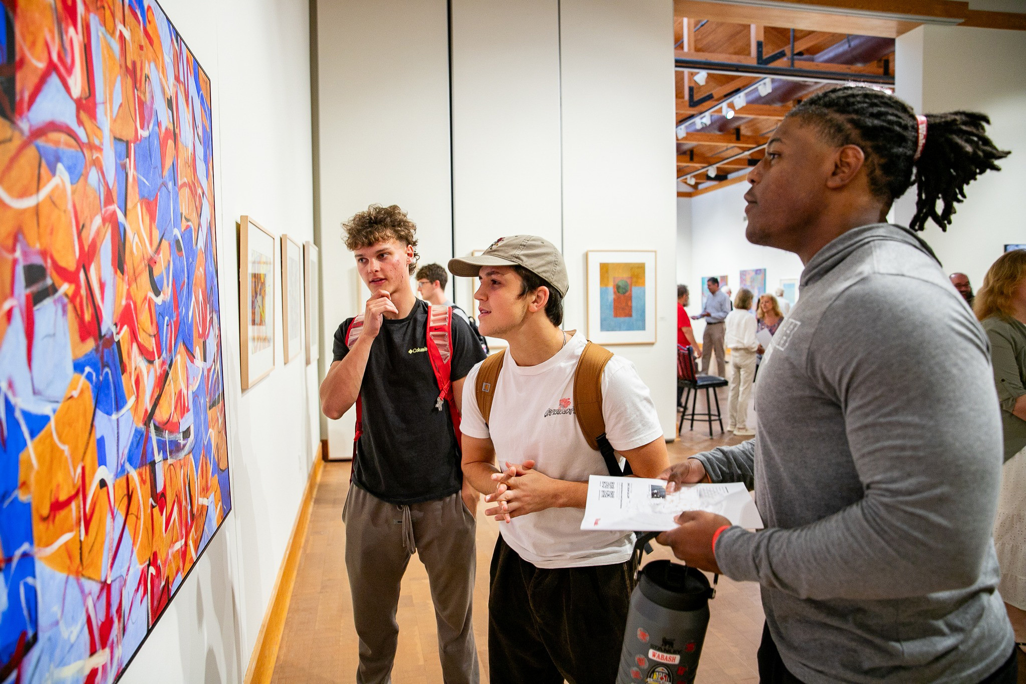 Silvio Radice ’26, Evan Dickey ’26, and Quinn Sholar ’26 examine a painting by Professor of Art Emeritus Greg Huebner H’77 during his retrospective show. 