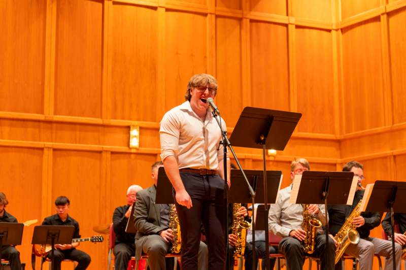 a man singing into a microphone with a group of people playing instruments