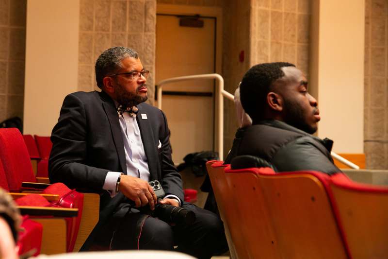 a man in a suit sitting in a room with other people