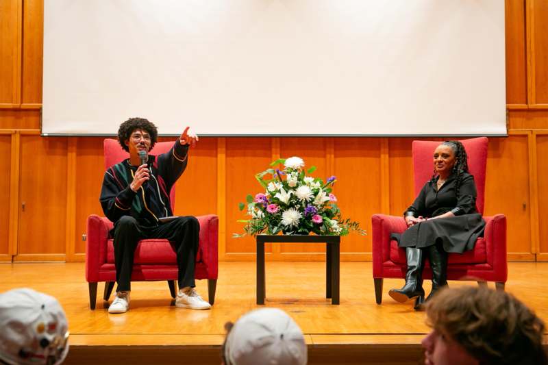 a man holding a microphone and sitting in chairs with a woman sitting in front of him