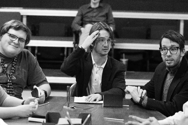 a man in a suit sitting at a table with other people in the background