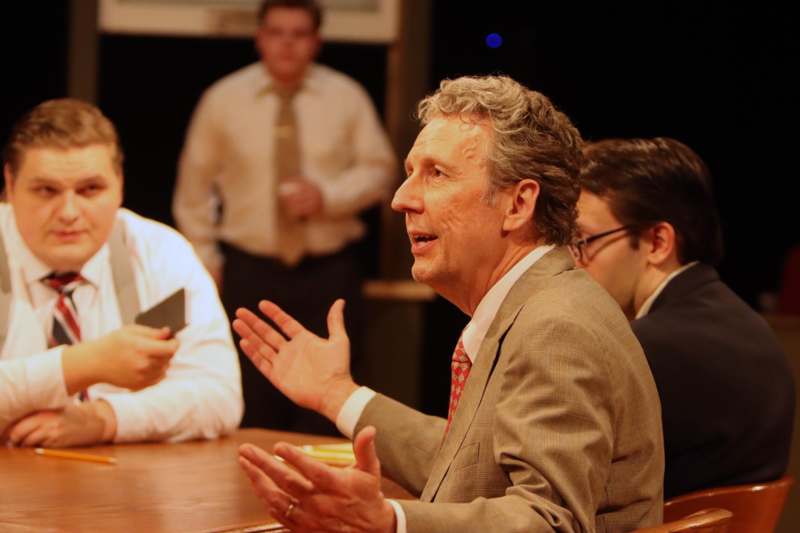 a man in a suit sitting at a table with other men in the background