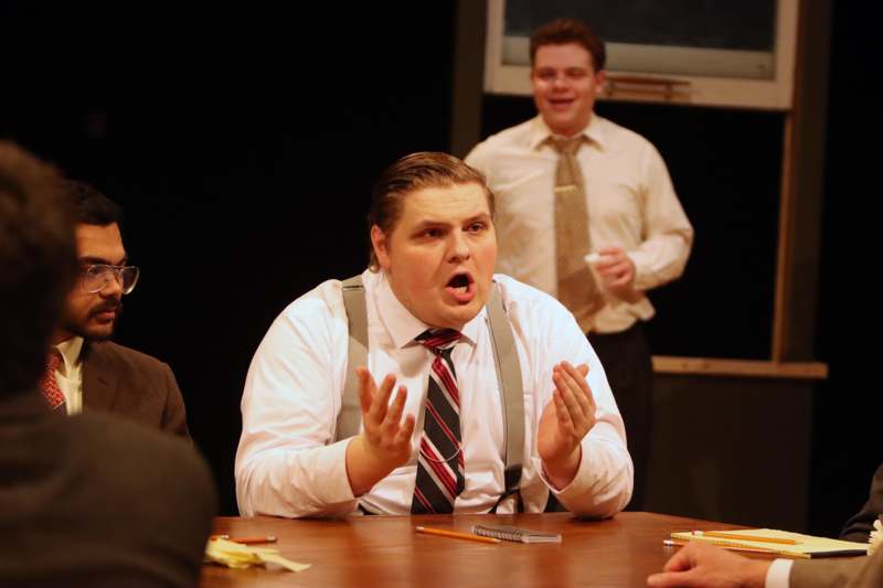 a man in suspenders sitting at a table with other men in the background