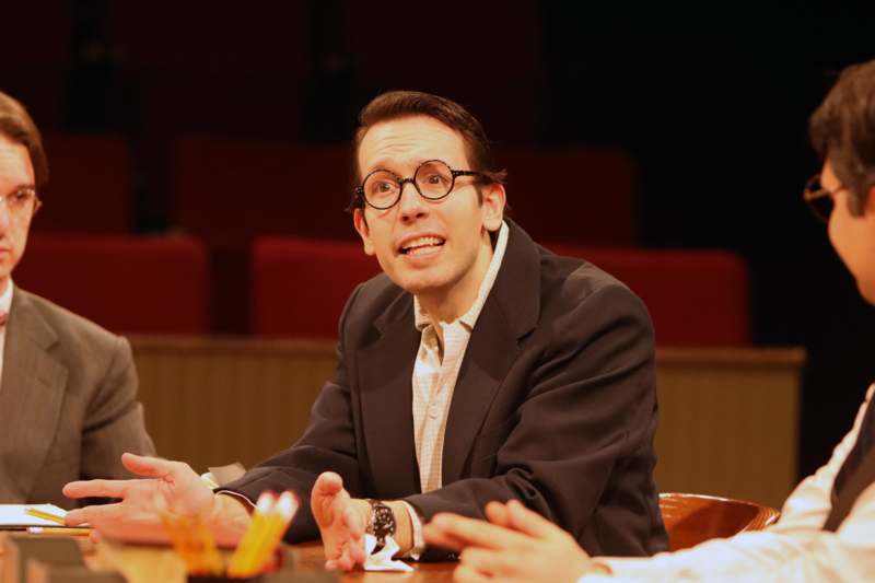 a man wearing glasses and a suit sitting at a table