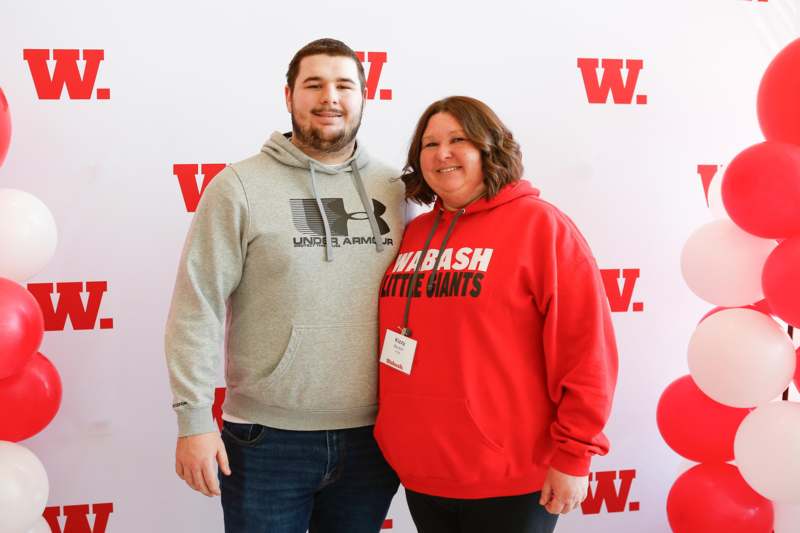 a man and woman standing together in front of a white wall with red letters