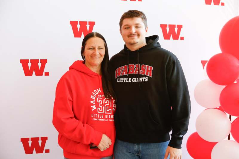 a man and woman standing together in front of a wall with red and white balloons