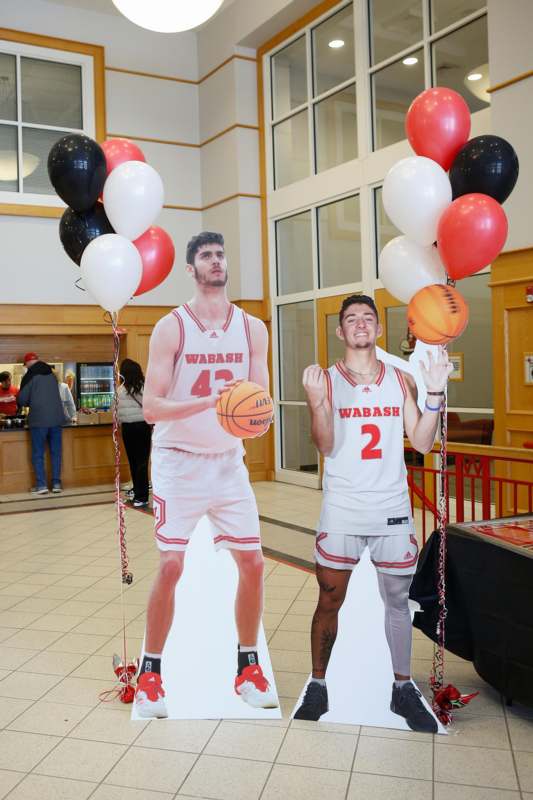 a man holding balloons and a cardboard cutout of a basketball player