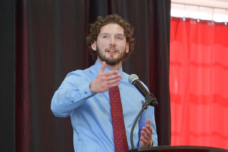 a man standing at a podium with a microphone and a red tie