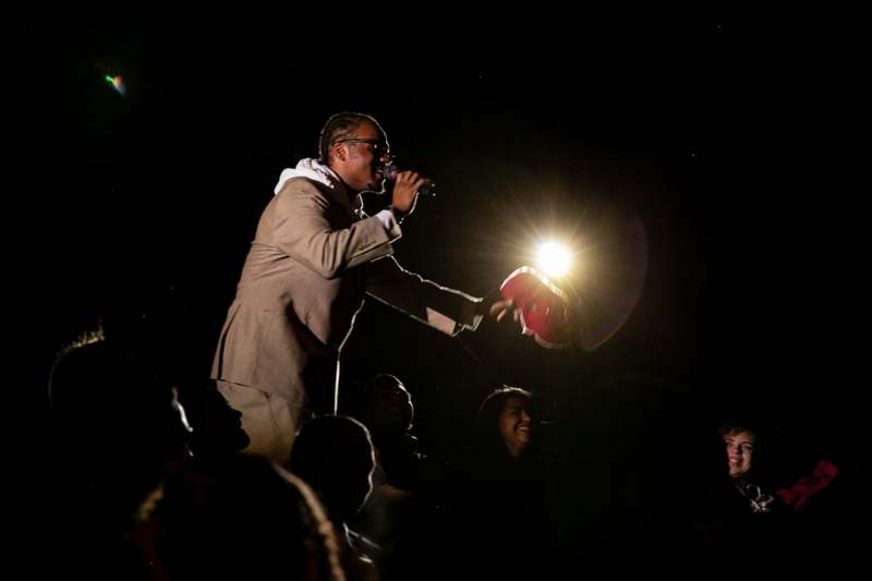 a man holding a microphone and standing in front of a crowd